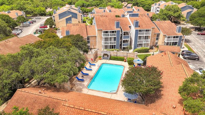 Charming aerial view of a vibrant apartment complex featuring pristine swimming pool, lush greenery, and stylish architecture with spacious balconies.
