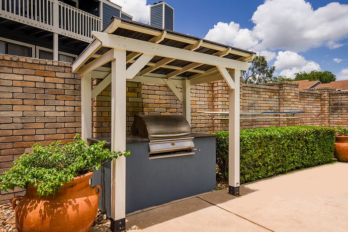 Elegant outdoor grilling station under a classic pergola, surrounded by lush greenery and tan brick walls, perfect for alfresco dining.