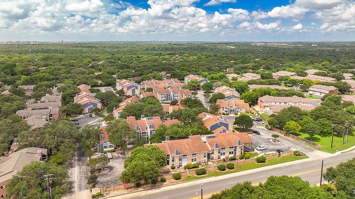 Charming aerial view of a vibrant apartment community nestled among lush green trees, showcasing red-roofed buildings with modern design.