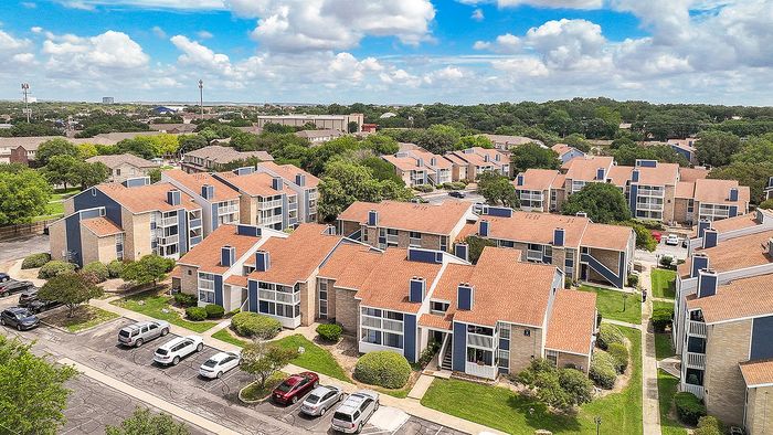 Scenic aerial view of a charming apartment complex with modern architecture, surrounded by lush greenery and ample parking.