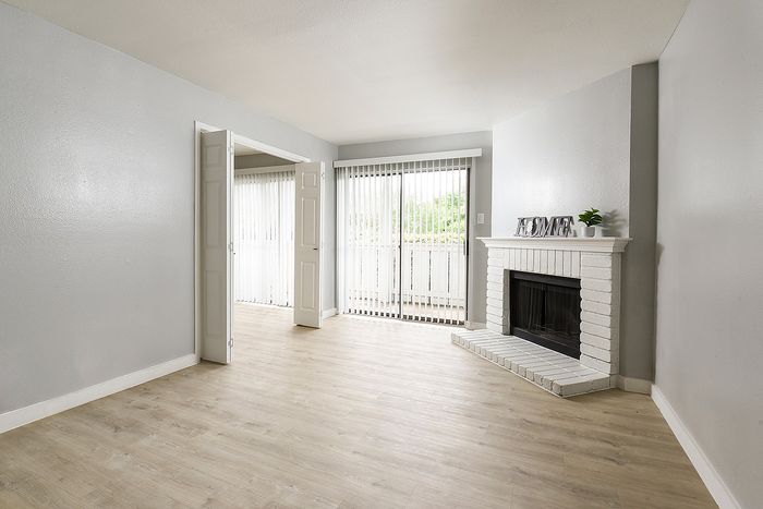 Bright and spacious living room with elegant grey walls, a cozy white brick fireplace, and large windows for natural light.