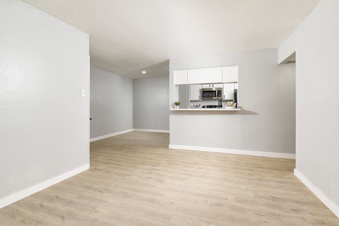 Modern open-concept living area with elegant hardwood flooring, featuring a sleek kitchen with stainless steel appliances and a breakfast bar.