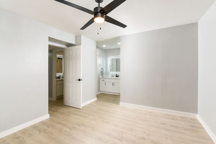 Bright and modern room with sleek ceiling fan, light wood flooring, and an elegantly designed bathroom entrance.