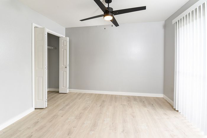 Sleek and modern empty apartment room with fresh gray walls, light wood flooring, and inviting natural light from large windows with vertical blinds.