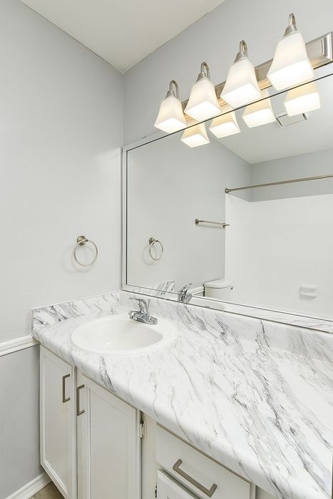 Elegant bathroom with a marble countertop, sleek fixtures, large mirror, and modern lighting.