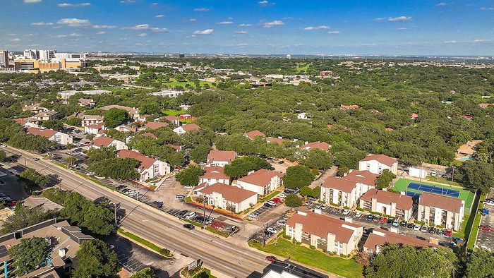 Aerial view of a vibrant suburban community with charming residential buildings surrounded by lush greenery and ample parking, offering easy access to urban amenities.