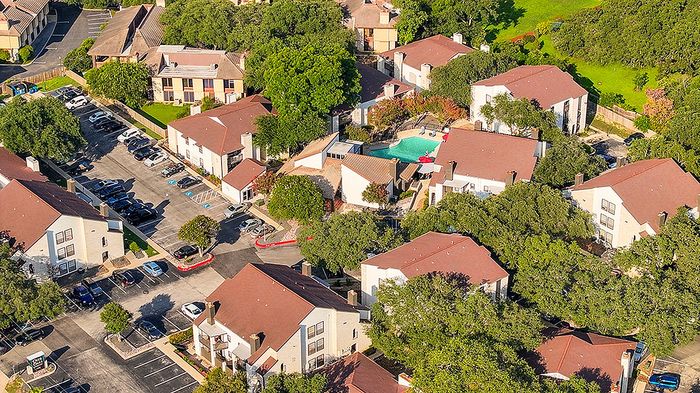 Charming aerial view of a residential community with red-roofed buildings, lush greenery, and a serene pool area.