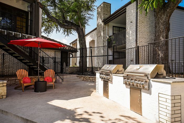 Charming outdoor patio with cozy seating under a vibrant red umbrella, featuring modern stainless steel grills for perfect al fresco dining.