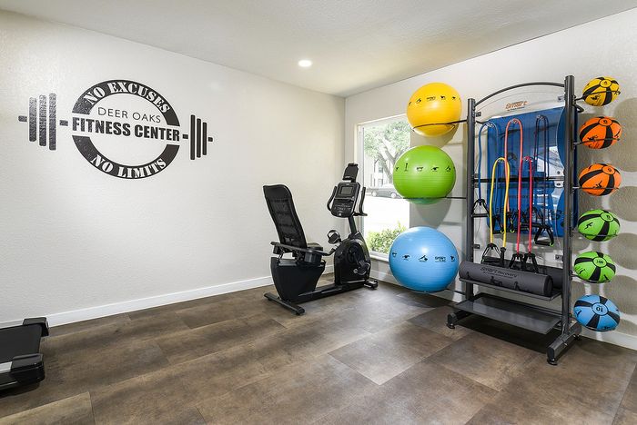 Modern fitness center with motivational wall art, featuring exercise equipment including a stationary bike, colorful stability balls, and resistance bands.