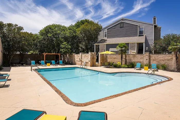 Inviting outdoor swimming pool surrounded by lush greenery and cozy lounge chairs, perfect for relaxation under a clear blue sky.