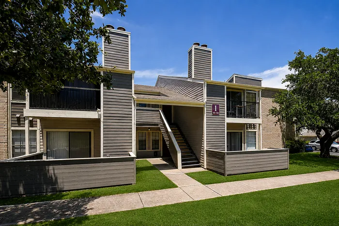Charming apartment complex with balconies, lush green lawns, and a modern design under a clear blue sky.