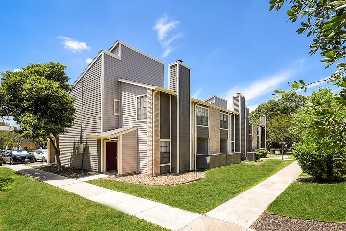 Charming townhouse exterior with modern design set against a bright blue sky, surrounded by lush greenery and a scenic pathway.