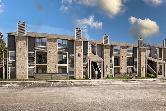 Charming apartment complex with modern design, featuring multi-level buildings and ample parking under a bright blue sky.