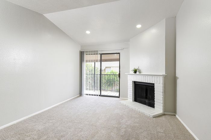 Bright and inviting living room featuring a modern white brick fireplace, plush carpet, and sliding glass doors leading to a charming balcony with outdoor views.