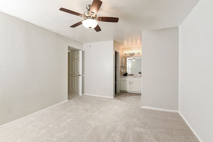 Bright and inviting bedroom with plush carpeting, ceiling fan, and attached modern vanity.