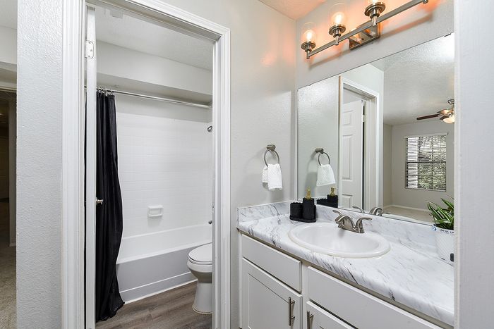 Elegant bathroom with marble countertop, modern lighting, and a pristine bathtub. Bright interior with large mirror and stylish decor, offering a serene and inviting space.
