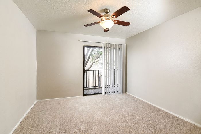Inviting bedroom with soft carpet flooring, ceiling fan, and a private balcony view through elegant sliding doors.