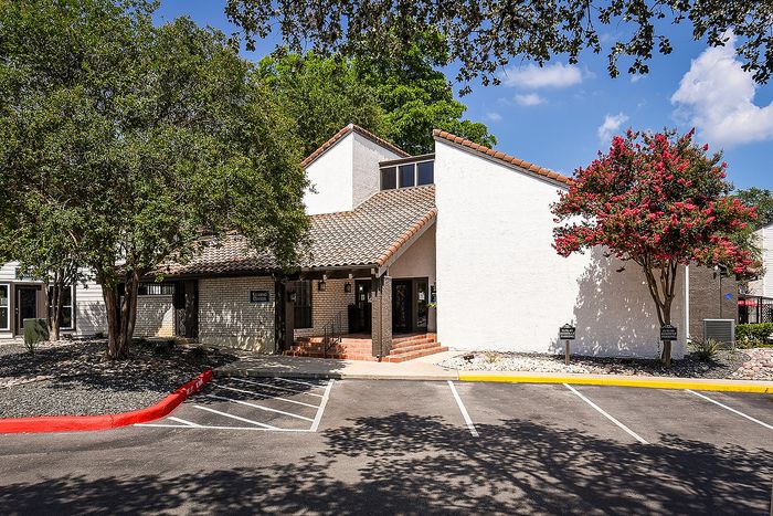 Inviting leasing center with charming architecture, set amidst lush greenery and vibrant flowering trees under a bright blue sky.