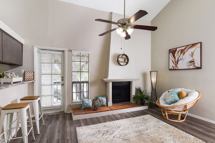 Charming living room with a cozy fireplace, modern ceiling fan, and inviting rattan chair accentuated by large windows for natural light.