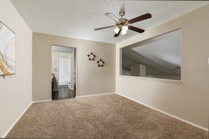 Cozy carpeted room with ceiling fan and window opening, adjacent to modern bathroom with wood flooring.