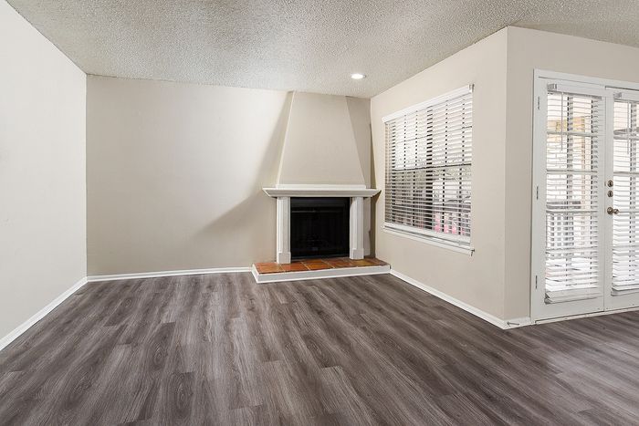 Inviting living room with elegant wood flooring, a cozy fireplace, and abundant natural light from large windows.