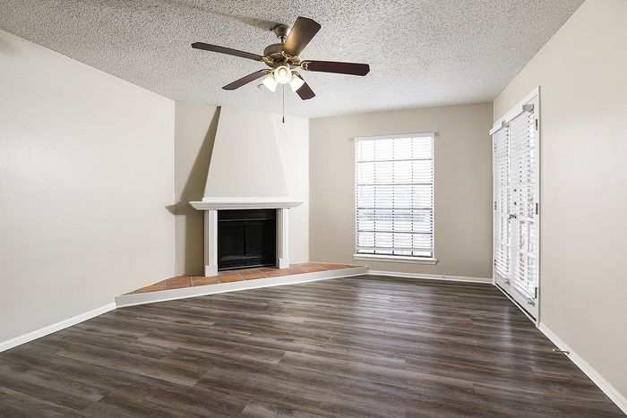 Contemporary living room with elegant fireplace, chic ceiling fan, and natural light from large windows and glass doors on sleek wood flooring.