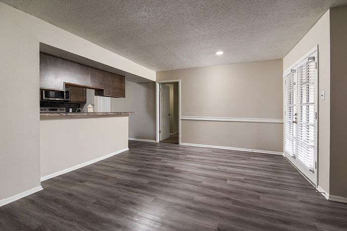 Modern open living area with sleek hardwood floors, flowing into an inviting kitchen with dark cabinetry and recessed lighting.