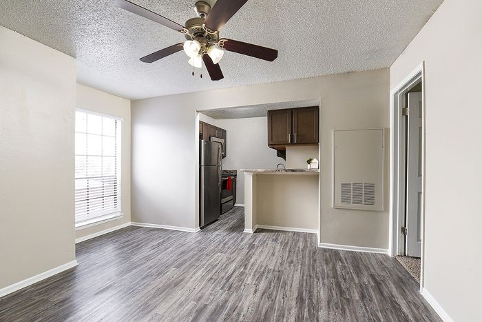 Modern living space with elegant gray wood flooring, showcasing an open-concept layout with a cozy kitchen area and a stylish ceiling fan.