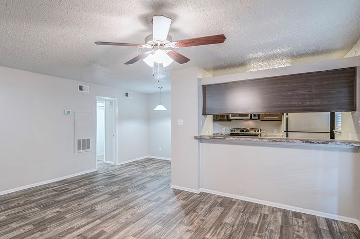 Modern open-plan living area featuring sleek wood flooring, a stylish ceiling fan, and a contemporary kitchen with stainless steel appliances.