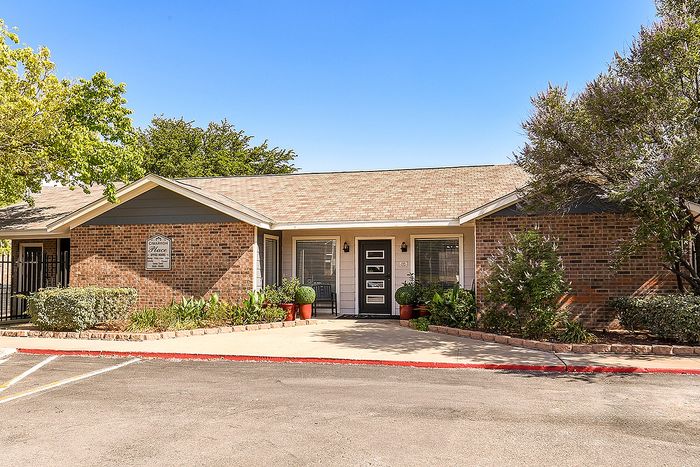 Charming suburban apartment with brick exterior, lush greenery, and inviting entrance, perfect for comfortable living.