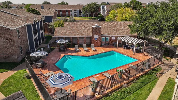 Charming apartment complex featuring a sparkling outdoor pool, cozy lounge chairs, and stylish umbrellas nestled amidst lush greenery.