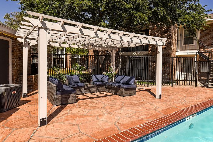 Charming outdoor patio with a stylish pergola and comfortable wicker seating by the poolside, perfect for relaxing and entertaining.