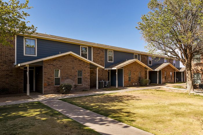 Charming brick apartment complex with modern design, surrounded by lush greenery and clear blue skies, offering peaceful living.