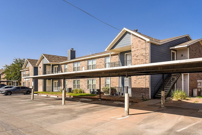 Charming apartment complex with brick facade and covered parking under a clear blue sky.