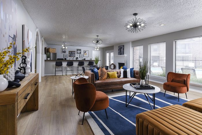 Chic and spacious living area with modern decor featuring a cozy leather sofa, stylish bar stools at an open kitchen, and vibrant natural light streaming in through large windows.
