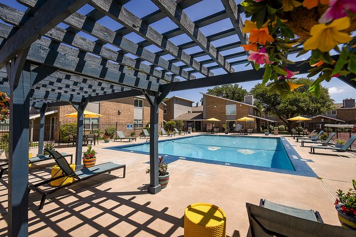Inviting community pool area with sun loungers under a charming pergola, surrounded by vibrant flowers and cozy seating.