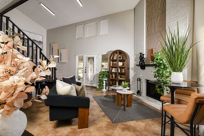 Modern living room with high ceilings, stylish decor, and cozy seating around a fireplace, featuring lush plants and contemporary art.