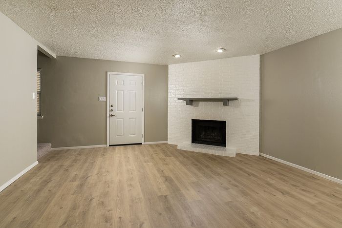 Inviting living room with sleek hardwood floors, a classic white brick fireplace, and ambient recessed lighting enhancing a warm atmosphere.