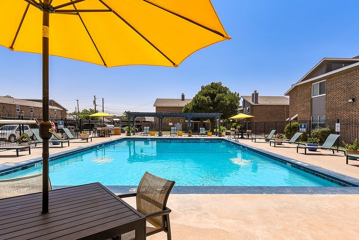 Inviting outdoor pool area with sun loungers and bright yellow umbrellas, set against a clear blue sky and modern apartment buildings.
