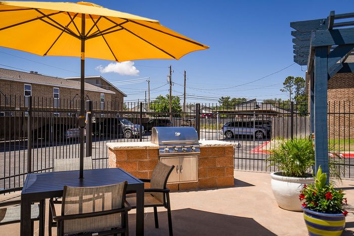 Charming outdoor patio area with a vibrant yellow umbrella, modern grill, and stylish seating, perfect for entertaining.