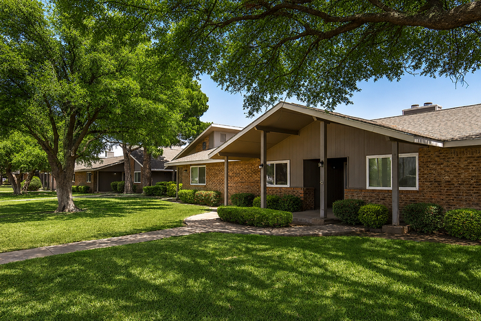 Charming residential community with lush green lawns, mature trees, and inviting front porches under a clear blue sky.