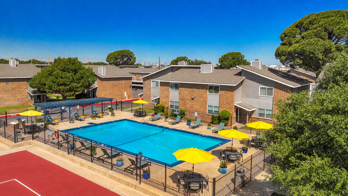 Inviting outdoor space featuring a sparkling swimming pool with vibrant yellow umbrellas, surrounded by comfortable lounge chairs and lush greenery in a modern apartment community.