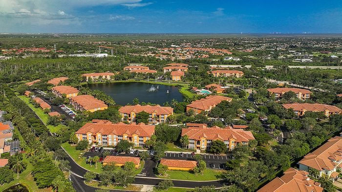 Breathtaking aerial view of a vibrant apartment complex surrounded by lush greenery and a serene lake, featuring charming orange-roofed buildings and inviting pathways.