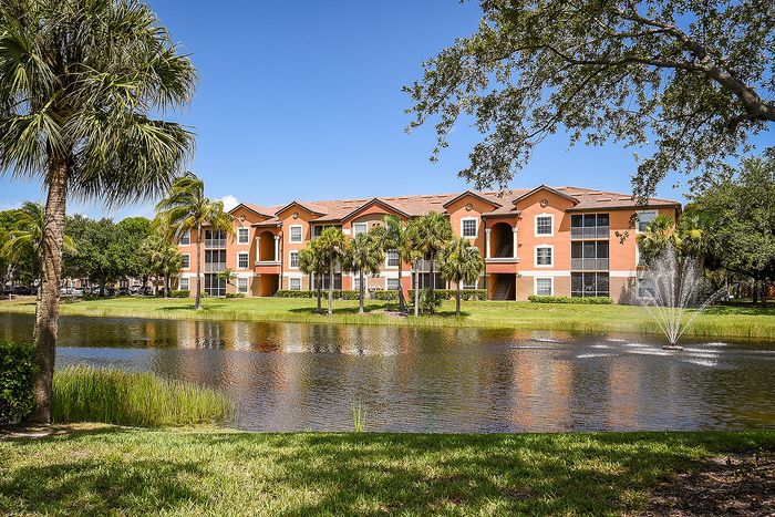 Charming apartment complex with picturesque pond view, surrounded by lush greenery and palm trees, ideal for tranquil living.