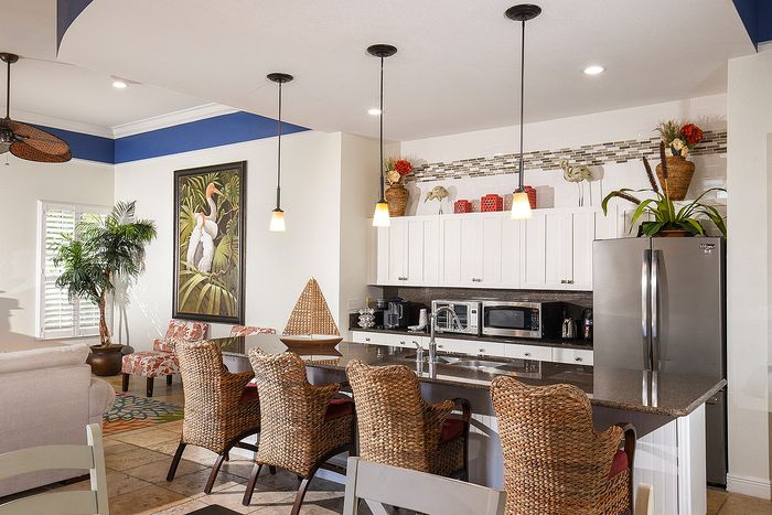 Charming kitchen with elegant wicker chairs, chic pendant lighting, and vibrant decor. Cozy seating area with tropical art and lush greenery adds a warm, inviting ambiance.