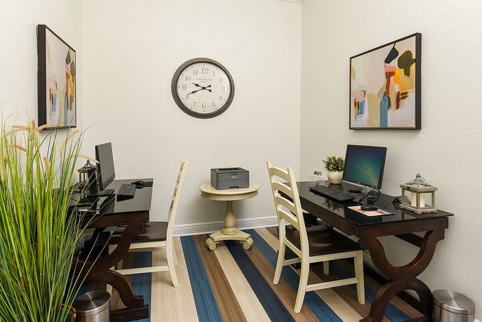 Bright home office corner with two elegant wood computer desks, modern decor, and a chic wall clock.