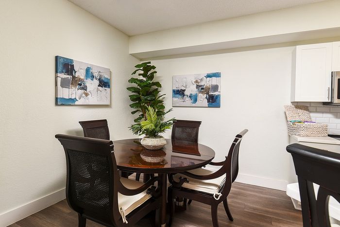 Elegant dining area with dark wood table, stylish chairs, vibrant art pieces, and lush green plant.