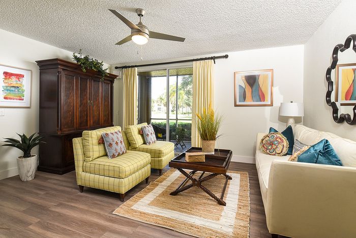 Charming living room with elegant decor, featuring cozy plaid armchairs, a modern ceiling fan, and sunlight streaming through large patio doors with scenic views.