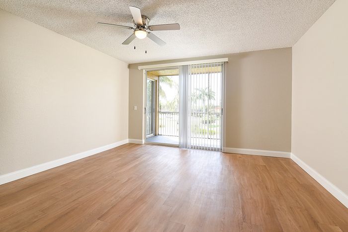 Bright and airy room with elegant hardwood flooring, ceiling fan, and sliding glass doors leading to a balcony with lush outdoor views.
