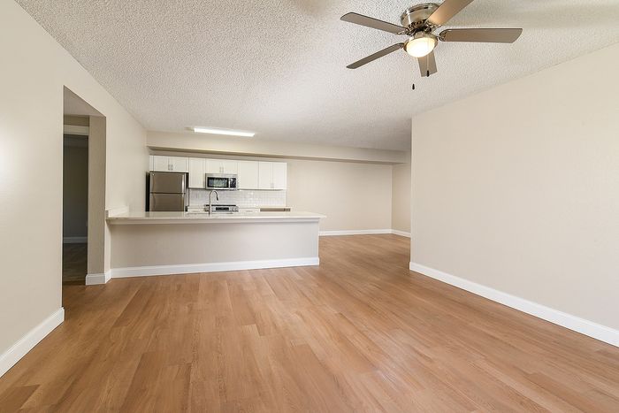 Bright open-concept living area featuring hardwood floors, modern kitchen with stainless steel appliances, and ceiling fan.